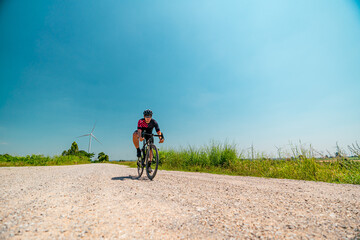 Fototapeta premium Cyclist rides on a gravel road surrounded by green fields and wind turbines under a clear blue sky
