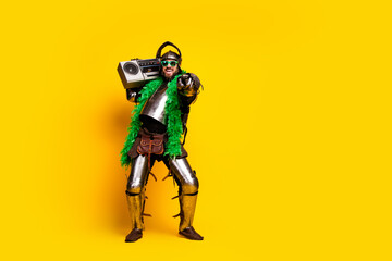 Young man in knight armor dancing with a boombox on vibrant yellow background showing a mix of historical and modern elements