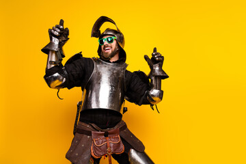 Fototapeta premium Young man dressed in medieval knight armor with modern sunglasses on a bright yellow background exuding fun and playfulness.