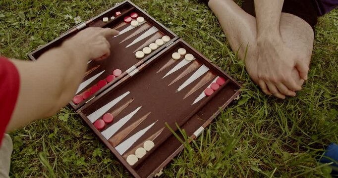 Two friends play backgammon in the park. A close-up shot of hands moving checkers on the board during a friendly game.