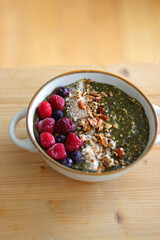 Beige bowl with green smoothie, frozen berries and homemade granola, served on the table. Selective focus.