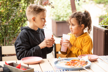 Cute girl and teenager boy eat pizza lunch in outdoor cafe and having fun.