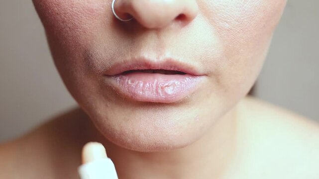 Woman with dry lips, Dry. She applies a moisturizing lip balm. close up. Cropped face
