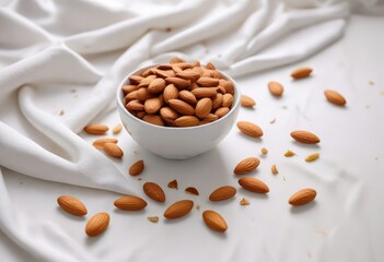 A bowl of almonds scattered across a plain white tablecloth, clean space, decorative element