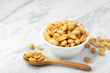 Peanuts in white bowl with wooden spoon on marble table background