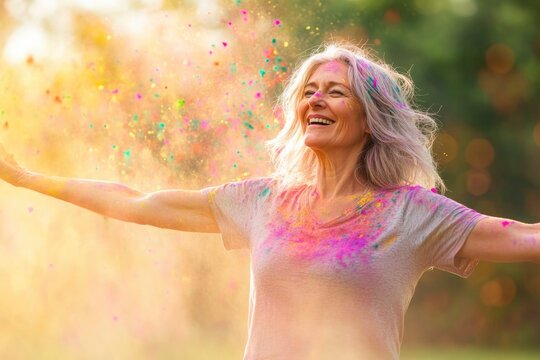 middle-aged woman dancing joyfully under cascade of colorful holi powders framed by vibrant sunlight