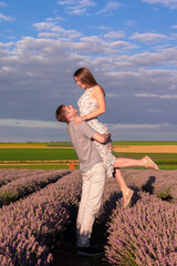 Joyful couple shares a romantic moment in a lavender field at sunset. The man is lifting the woman in the air as they smile warmly to each other