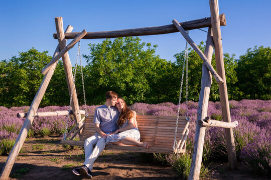 Lovely couple sits on a rustic wooden swing amidst lavender field during a sunny summer day - Powered by Adobe
