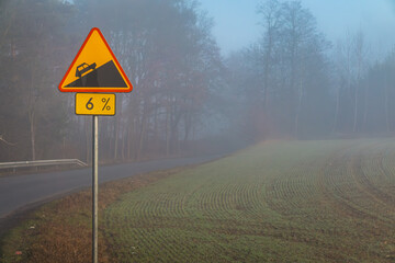 road during morning fog. Bad weather conditions while driving will occur in autumn and winter. poor visibility on the road. road sign warning about 6% elevation in the mountains.