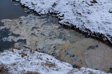 biological contamination of water in a small river. floating yellow goo on the water surface. stinking water in the river. releasing waste into the river in winter