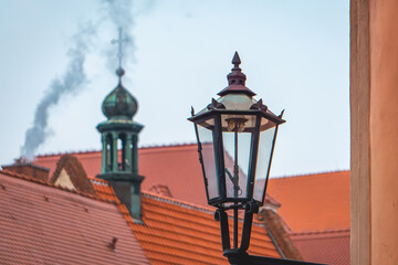 urban architecture in the old town of Wroclaw. old historic beautifully decorated buildings. a classic street lamp against the background of a church tower and a smoking chimney in the distance