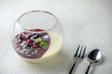 A panna cotta with berry sauce and mint on a white table