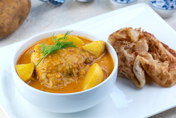 A bowl of yellow curry with chicken, potatoes, and roti