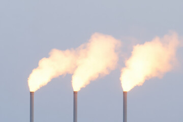 Three tall smoke stacks are spewing out thick, yellow smoke