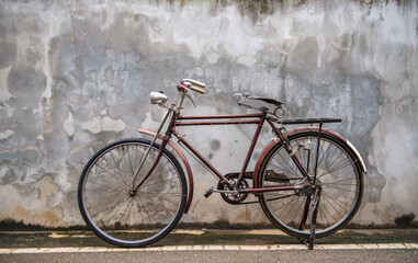 Vintage bicycle on old rustic dirty wall house, many stain on wood wall. Classic bike old bicycle on decay brick wall retro style. Cement loft partition and window background.