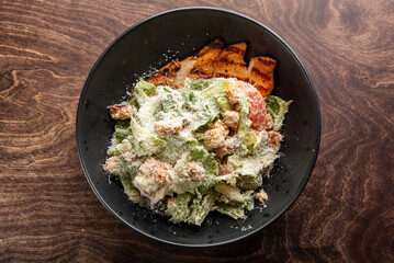 A fresh and colorful Caesar salad in a black bowl, featuring crisp romaine lettuce, grilled chicken, croutons, and a sprinkle of Parmesan cheese