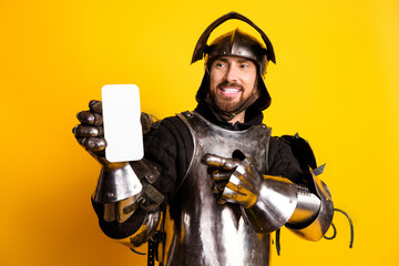 Smiling knight wearing armor holding smartphone with a yellow background