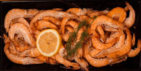 Delicious boiled shrimp with a slice of lemon and a sprig of dill on a black background. Perfect for culinary content and seafood themes.