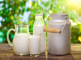 Decanter, bottle and glass of milk on wooden table and blurred green nature background.