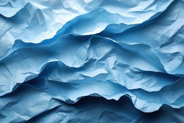 Fototapeta premium Crumpled blue paper texture creating a wave-like pattern under soft light