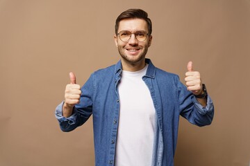 Young man with glasses smiling and giving thumbs up against a plain background indoors