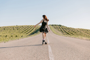 Obraz premium Young woman in dress riding on roller skates outdoor on sunny day