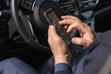 Close-up of a mature man's hands holding a smartphone inside a car. The image conveys themes of technology, communication, and modern lifestyle, with a focus on detail and functionality.