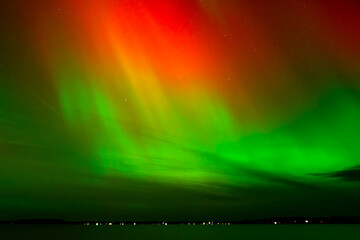 Vibrant red and green auroras (Northern Lights) paint the night sky, creating a mesmerizing and surreal atmosphere over Grand Traverse Bay, Michigan, USA.