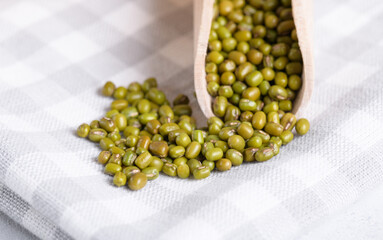 Mung beans in wooden scoop on cotton napkin, close up