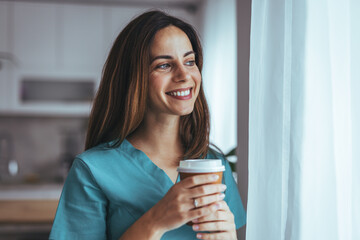 Smiling Woman Enjoying Coffee While Standing by a Window at Home