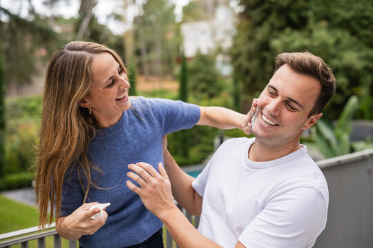 Playful couple applying sunscreen or exfoliating cream on balcony - Powered by Adobe