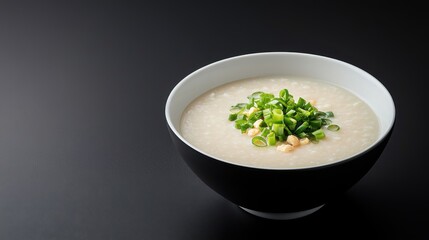 Creamy Rice Congee Bowl with Fresh Chopped Green Onions on Smooth Black Background