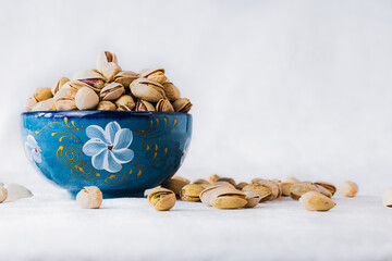 Pistachios in a blue bowl on white background with copy space. Healthy snack, nuts, food photography.