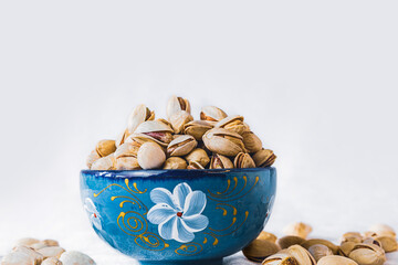 Pistachios in a blue bowl on white background with copy space. Healthy snack, nuts, food photography.