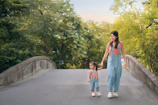 Asian mother walking with daughter in park, Parents hold the baby's hands, Happy family in the park evening light. Happy family concept;