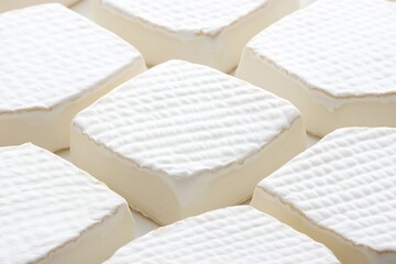 Close-up of multiple square-shaped creamy white cheeses with textured rind arranged in a repeating pattern.