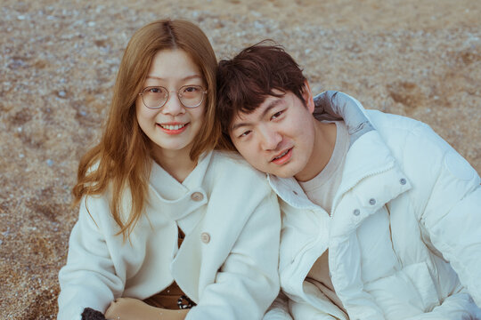 Couple sitting on pebble beach. 
Young couple wearing winter outfit sitting on pebble beach.