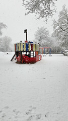 Naklejka premium A red boat is covered in snow. The boat is in a park with a playground.