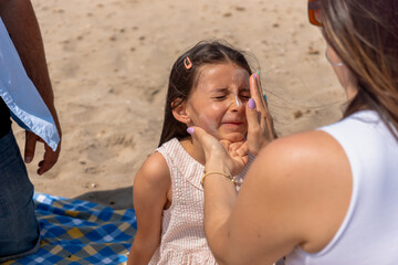 Fototapeta premium Mom carefully applying sunscreen to her daughter's face during a sunny day at the beach
