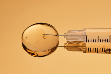 A syringe with a drop of a medical drug on a golden background.