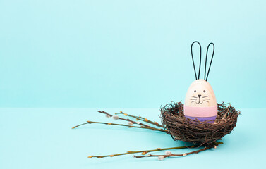 Easter bunny or rabbit sitting in a bird wicker nest, willow branches, wooden egg, spring holiday, brown and blue color 