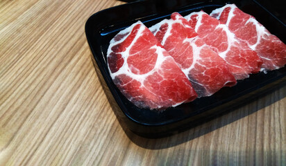 Fresh sliced meat or pork in black tray or dish on wooden table with copy space. Uncooked food on wood background.