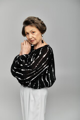 A beautiful woman in her 60s elegantly poses in sophisticated attire, exuding timeless fashion.