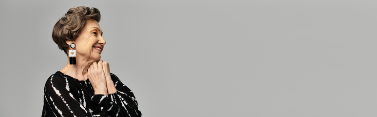 A beautiful woman in her 60s poses gracefully in elegant attire against a grey background, banner