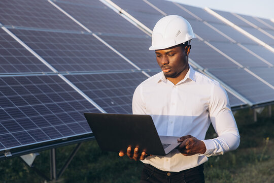 African American Engineer Inspecting Solar Panels With Laptop On Site