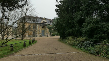 Historic mansion surrounded by greenery along a gravel path on a cloudy day in France.