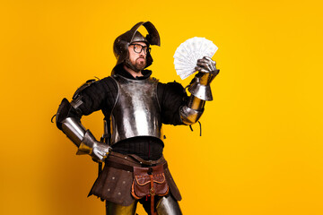 Fototapeta premium A young man in medieval knight costume holding money on a vibrant yellow background