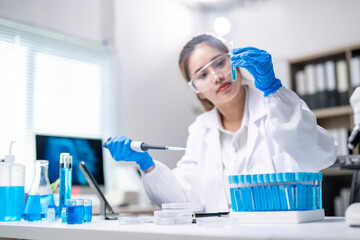 A woman in a lab coat is holding a blue liquid in a test tube