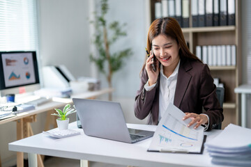 A woman is talking on her cell phone while sitting at a desk with a laptop