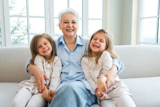 Happy family at home. Two little girls sisters twins grandmother enjoying time together. Good time at home. Grandma granddaughters child kids emotional bonding hugging together. Family generations - Powered by Adobe